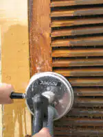 Koristeći Mosmatic FL-ABB 200 povrsinski čistač i crevo, neko čisti drvene kapke uokvirene žutom bojom, sa vidljivim sapunom i vodom.