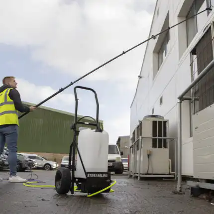 Radnik u žutom zaštitnom prsluku čisti prozore koristeći Streamflo 25L sistem za čišćenje na točkovima, sa crevima i rezervoarom, sa oznakom STREAMLINE.