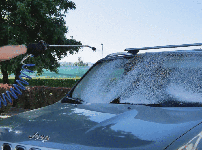 Osoba u crnoj rukavici koristi Profi mašinu za auto-detailing Biemmedue EX-F 80 i prska sapunicu po vetrobranu plavog Jeep SUV-a na suncu.