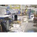 Velika industrijska hala sa mokrim podom, dva BIEMMEDUE DR70 odvlaživača i radnik u plavom pored opreme i polica.