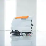 Mašina za čišćenje podova CHANCEE M50+ sa belim telom i narandžastim vrhom stoji na sjajnom svetlom podu u modernoj prostoriji.