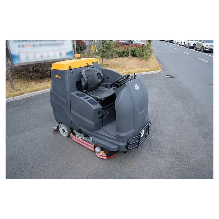CHANCEE K100 vozeća mašina za pranje podova sa crnim sedištem i žutim detaljima stoji na asfaltu; u pozadini su trava, žbunje i automobili.
