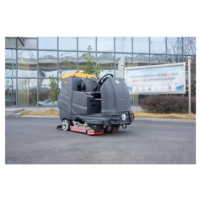 Crno-žuta CHANCEE K100 vozeća mašina za pranje podova stoji na ploči ispred staklene zgrade i nejasnog znaka.