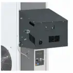 Detaljan prikaz industrijske mašine sa crnom metalnom kontrolnom kutijom, rešetkama za ventilaciju, ručkom, bravom na ključu i dugmadima; veliki ventilator se delimično vidi levo.