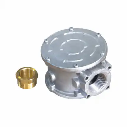 Na beloj podlozi se nalazi srebrno metalno telo ventila sa okruglim poklopcem i navojima, pored mesinganog priključka.